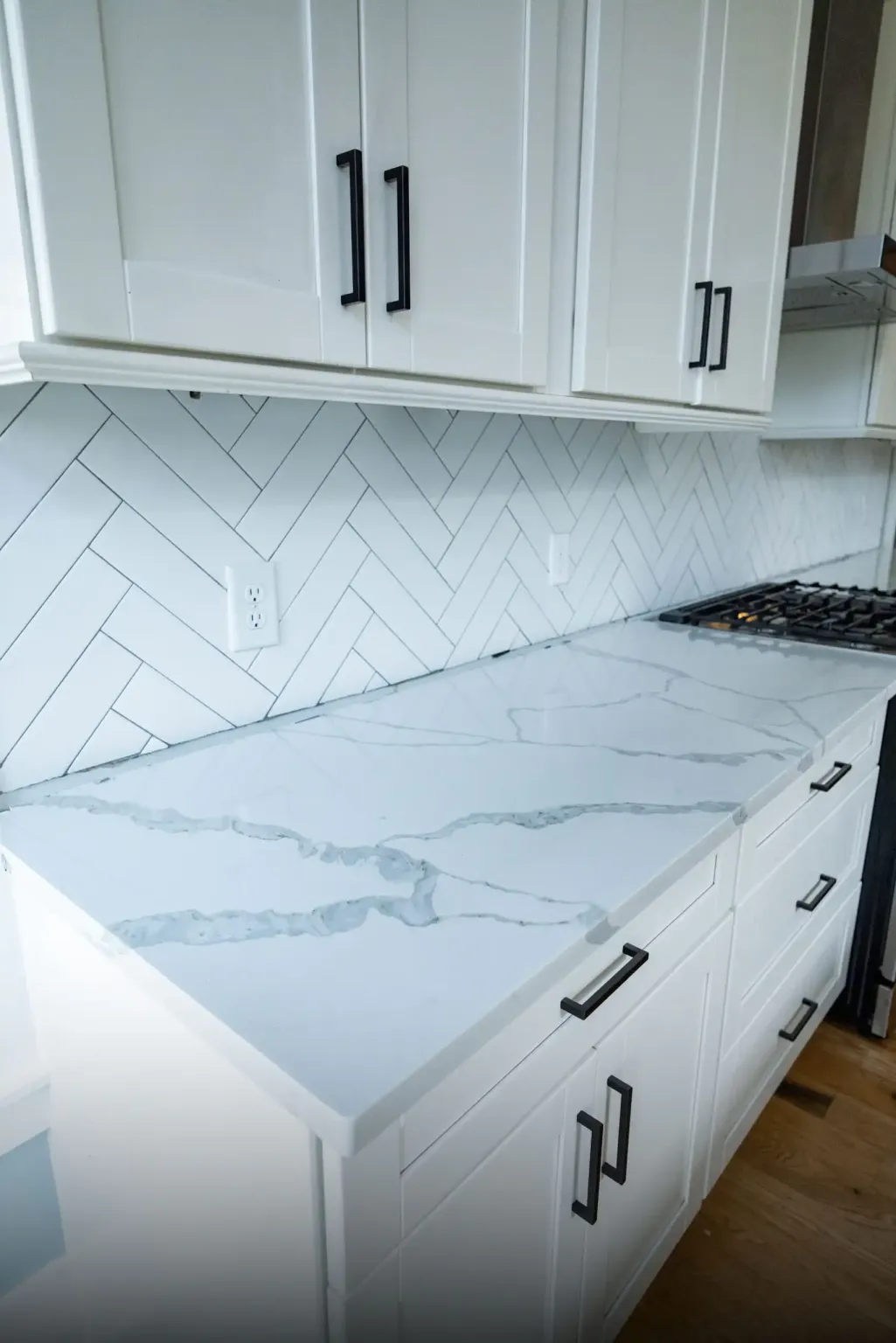 White countertop with soft gray veining on white shaker cabinets with matte black pulls and a herringbone tile backsplash, Moncks Corner kitchen