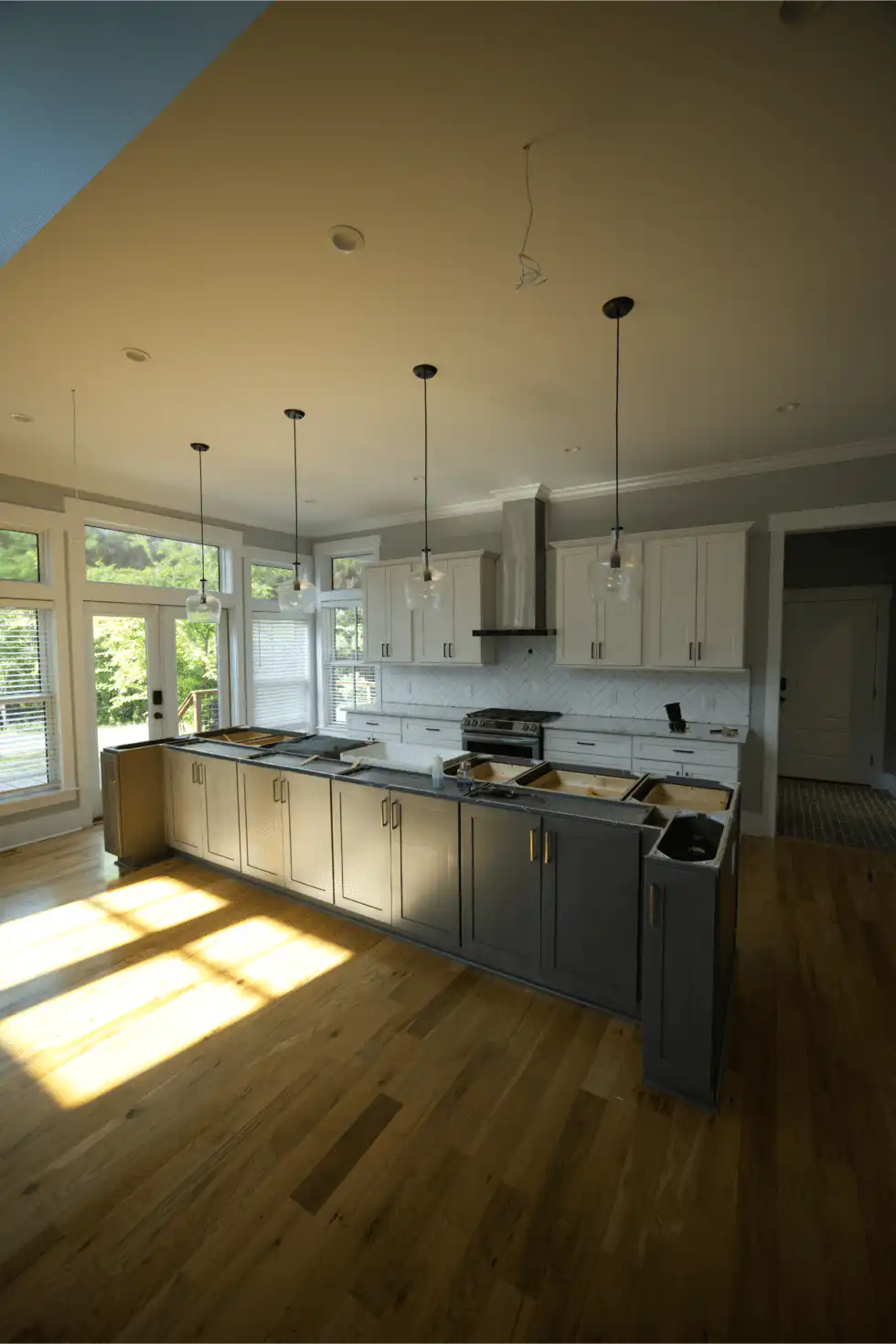 Two-Tone Kitchen Countertops: How to Pair Two Stones That Work Together Kitchen with a long gray-painted island and white perimeter cabinets, the island still waiting for its stone top, pendant lights above
