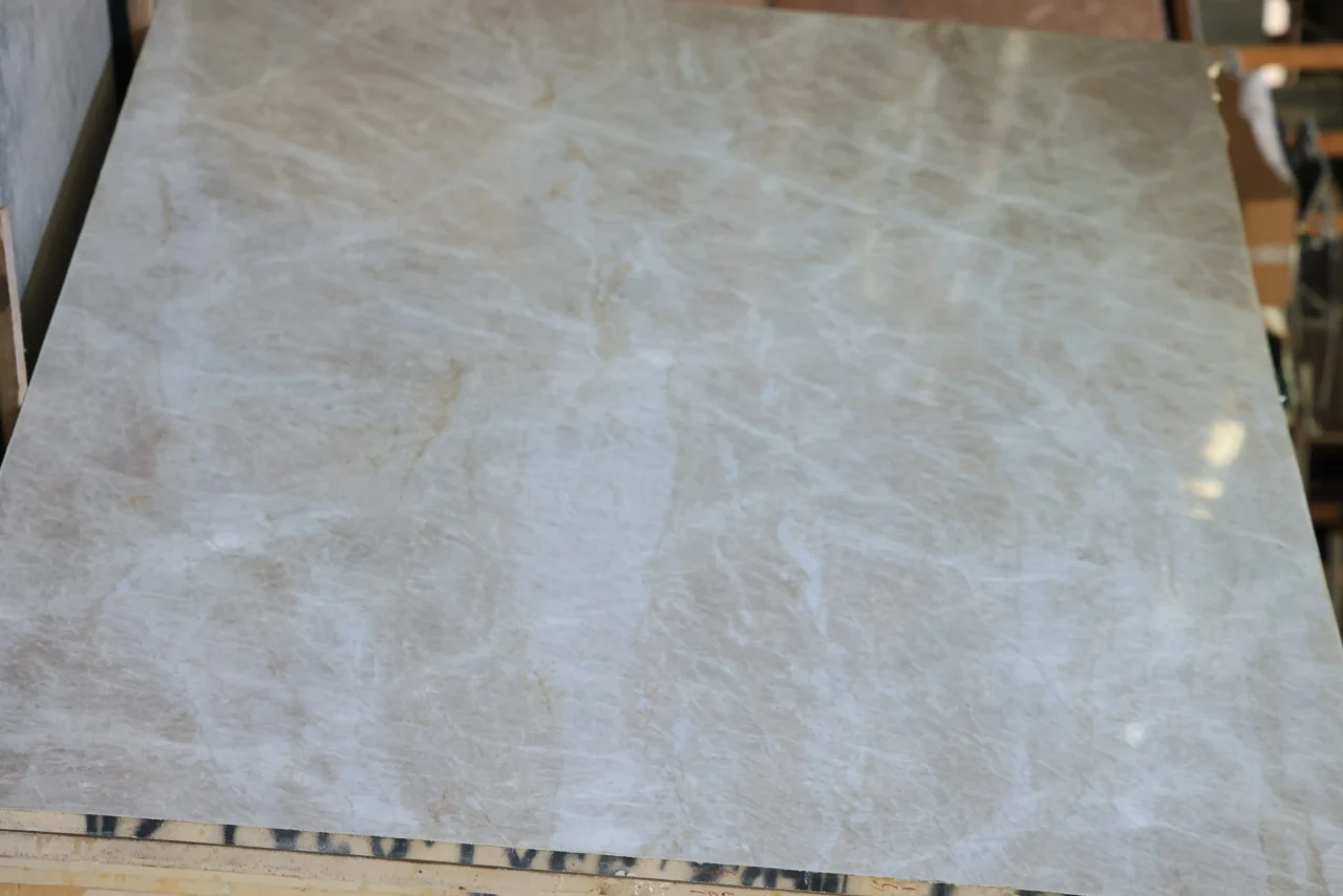 Polished Taj Mahal quartzite slab, warm beige with a fine web of white veining, leaning on a rack in the Stonhaus slab warehouse