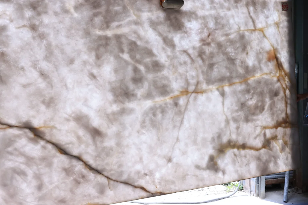 Crystallo quartzite slab lifted outdoors by a vacuum lifter, milky white body crossed by amber and dark veins