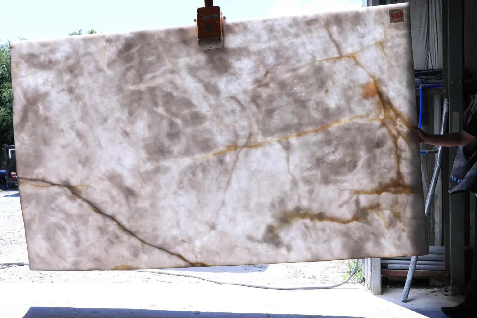 Crystallo quartzite slab held by a vacuum lifter outdoors, with amber and gray veins across a translucent white body