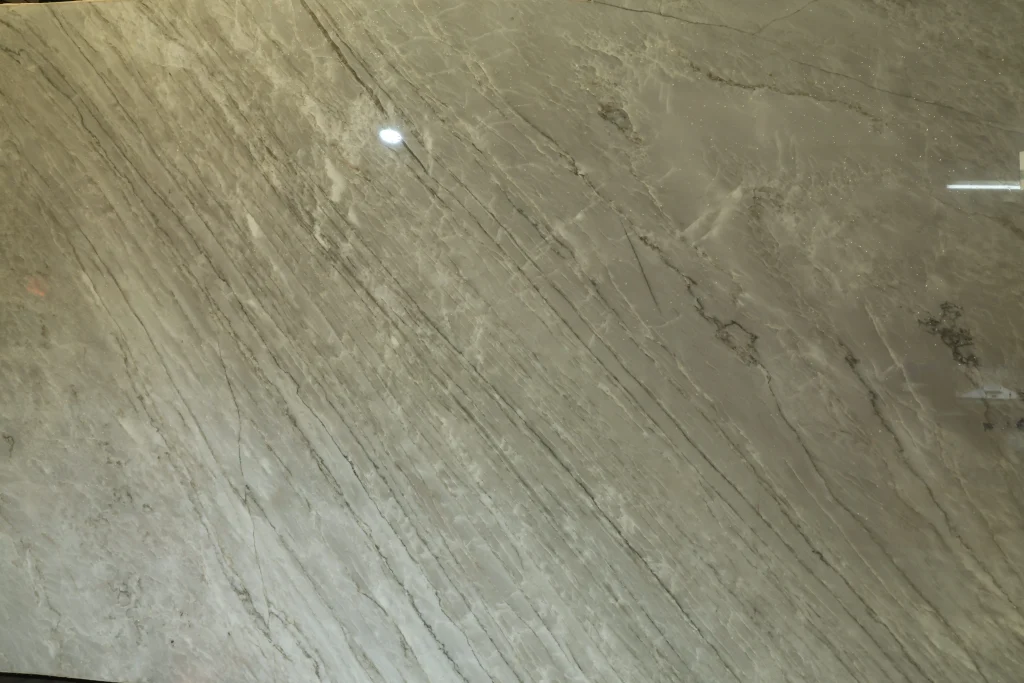 Close view of a Sea Pearl quartzite slab under warehouse lights, showing long thin gray veins across a pale surface