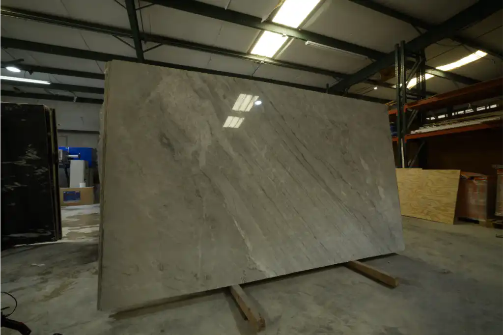 A full polished natural stone slab standing upright under overhead warehouse lights