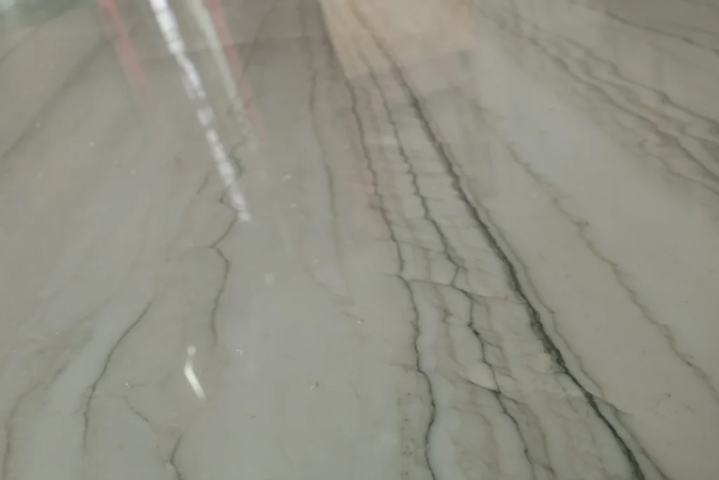 Close view of a pale gray-white polished stone with charcoal veins running in fine parallel lines