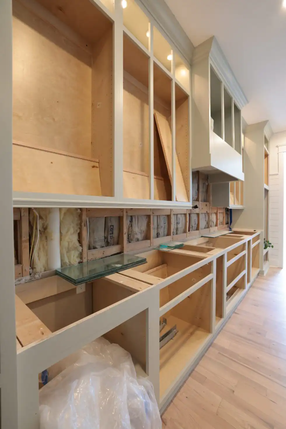 Row of painted base and wall cabinets installed without countertops, with the wall behind still open to studs and wiring