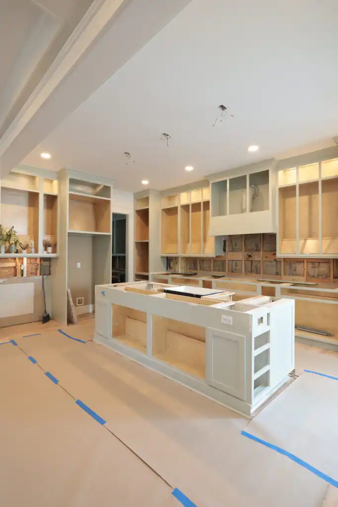 Kitchen with island and perimeter cabinets installed and open on top, floor covered with protective paper and blue tape, ready for countertop templating